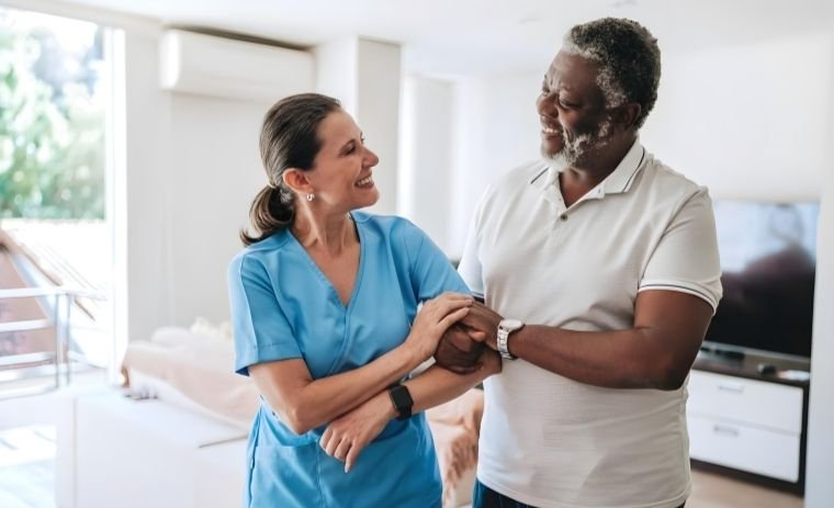 Professional home health care aide smiling and supporting a senior man at home, showing compassionate and trusted caregiving.
