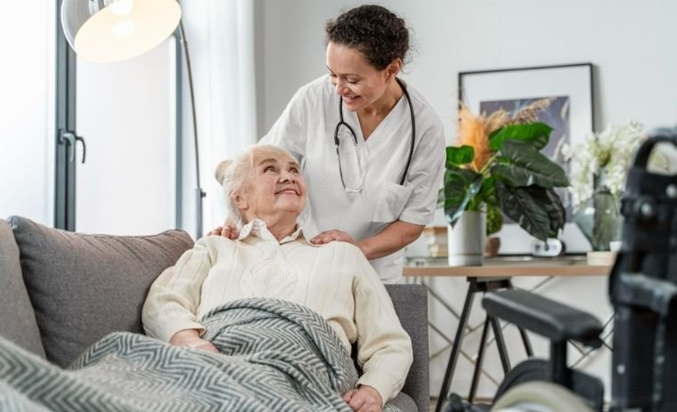 Smiling nurse providing home health care in New Jersey to a senior woman sitting on a couch, showing comfort and professional in-home support