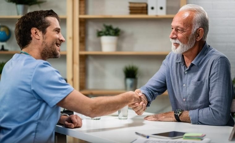 A caregiver from a senior home care agency in New Jersey warmly shaking hands with an elderly man during a home care consultation, representing trust and compassionate senior home care services