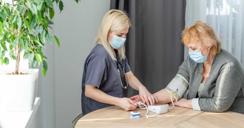 A personal care assistant providing PCA services checks an elderly woman’s blood pressure at home, supporting chronic illness management in New Jersey.