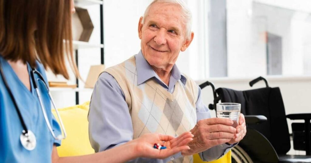 Caregiver assisting an elderly man with medication reminders at home as he holds a glass of water, supporting safe health monitoring.