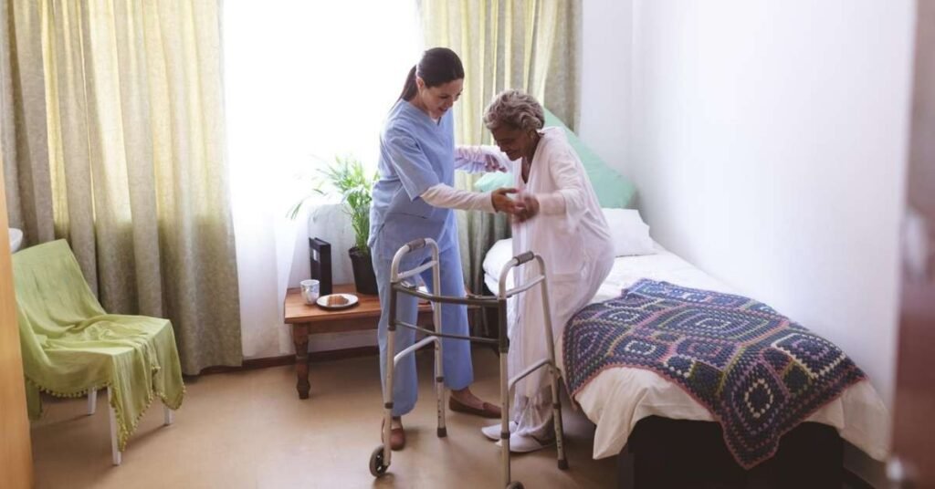 Home health caregiver assisting an elderly patient with a walker at home to support safe mobility and recovery after hospital discharge.
