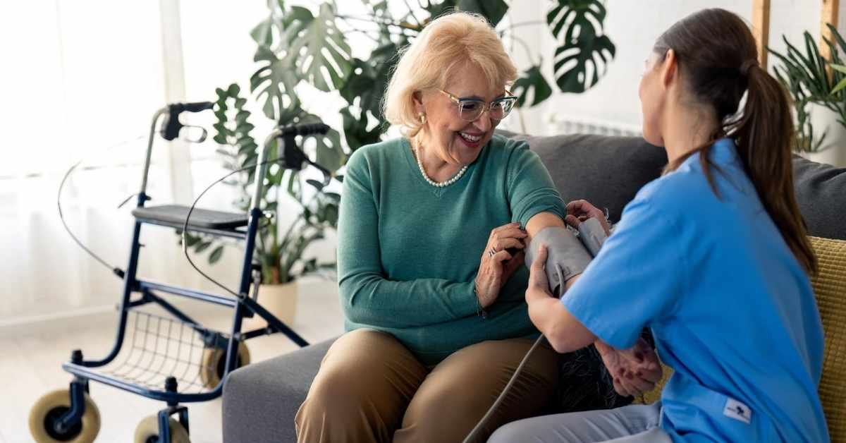 Home health care nurse providing skilled home health care services by checking blood pressure for an elderly woman at home.