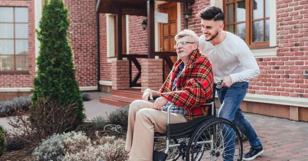Senior man in wheelchair receiving home health care support from caregiver outside home, representing long-term home care assistance in New Jersey.